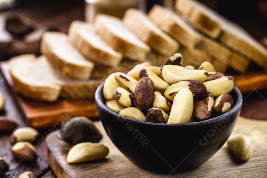 Castanhas-do-pará em tigela escura com pão fatiado ao fundo