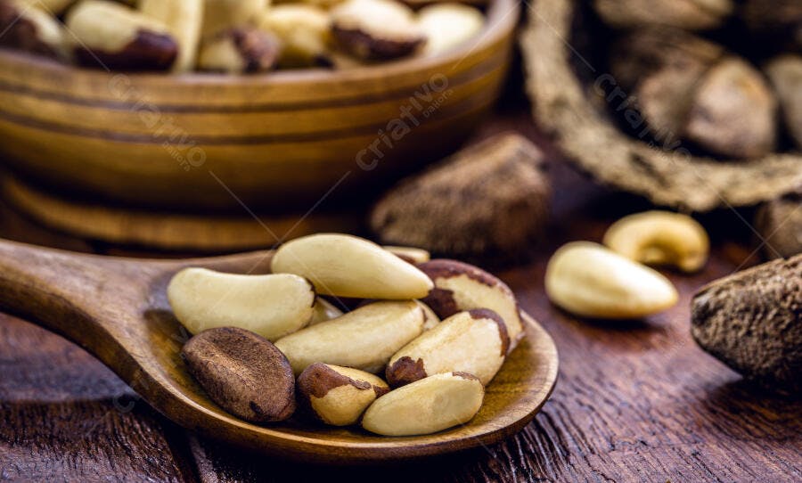Castanhas do Pará descascadas e com casca em colher de pau rústica sobre madeira escura