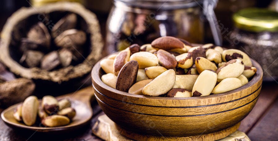 Castanhas do Pará em tigela de madeira com cascas ao fundo tons de marrom e creme