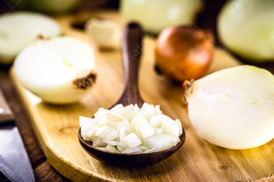 Cebolas brancas e marrons picadas em colher de pau sobre tábua de madeira