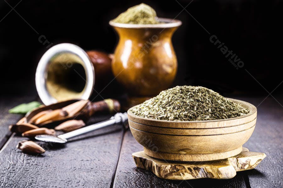 Erva-mate em tigela de madeira com cuias e pinhões para chimarrão na mesa escura