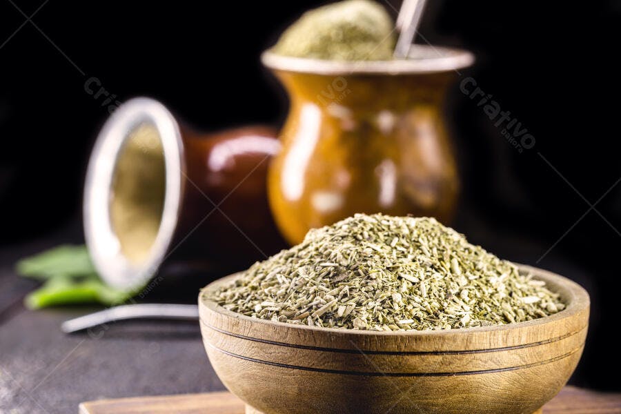 Erva-mate verde em tigela de madeira com cuias em fundo escuro