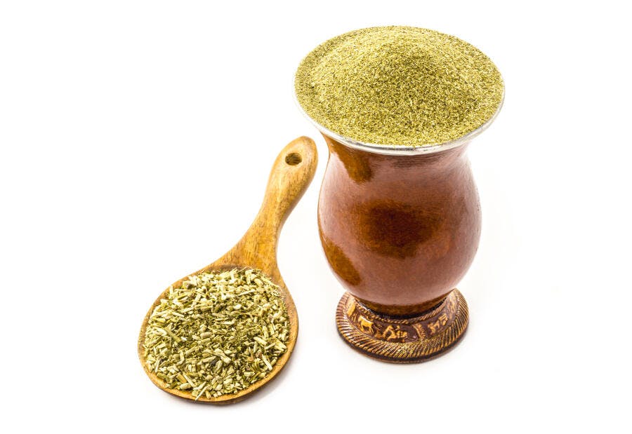 Erva-mate verde na cuia tradicional e colher de pau em fundo branco