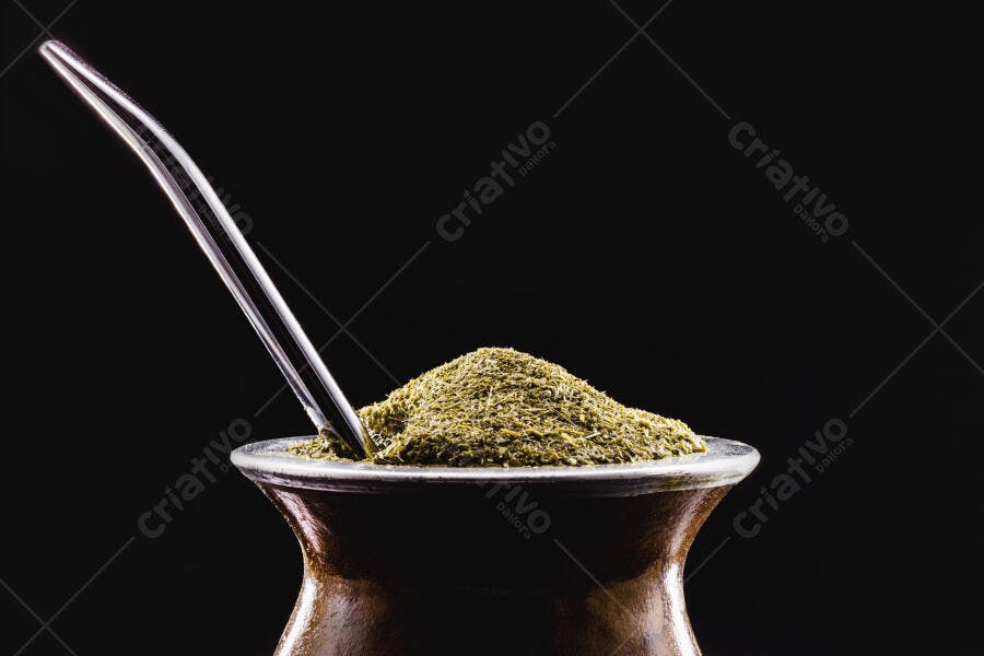 Cuia de chimarrão com erva-mate verde e bomba prateada em fundo preto