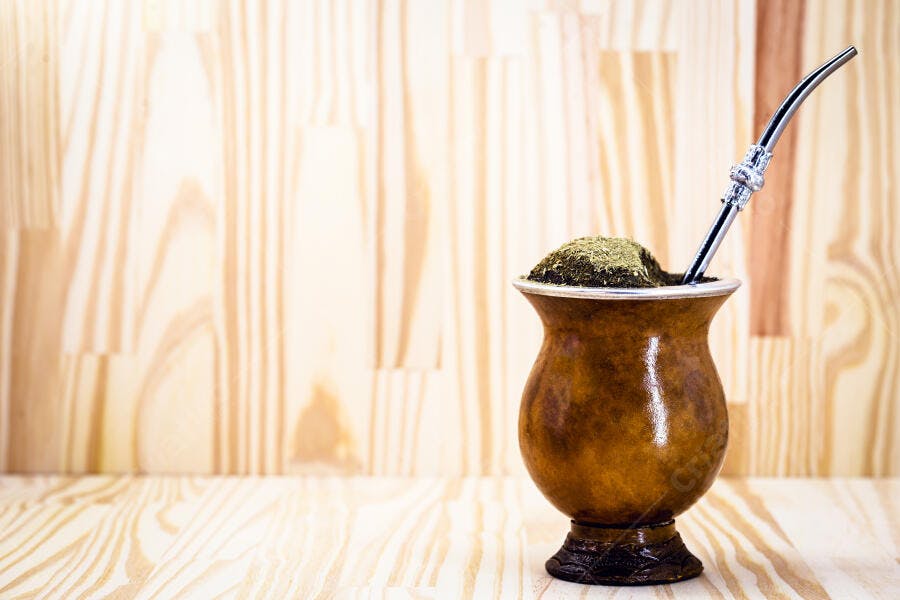 Cuia de chimarrão com erva mate e bombilla prata sobre mesa de madeira