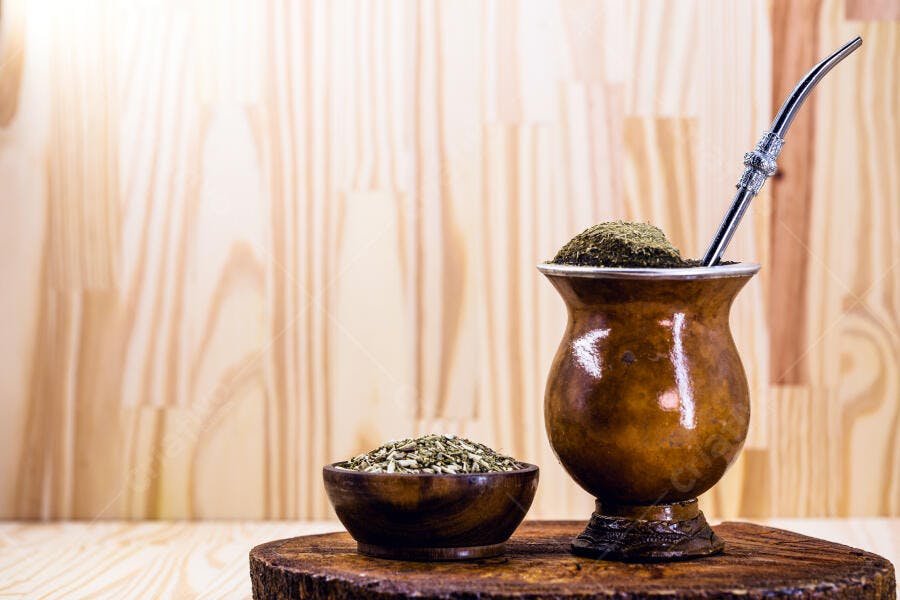 Chimarrão tradicional e erva mate em cuia e tigela de madeira rústica