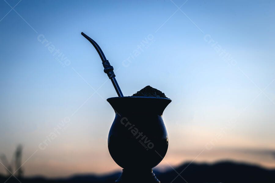 Cuia de chimarrão com bomba em silhueta ao amanhecer céu azul laranja