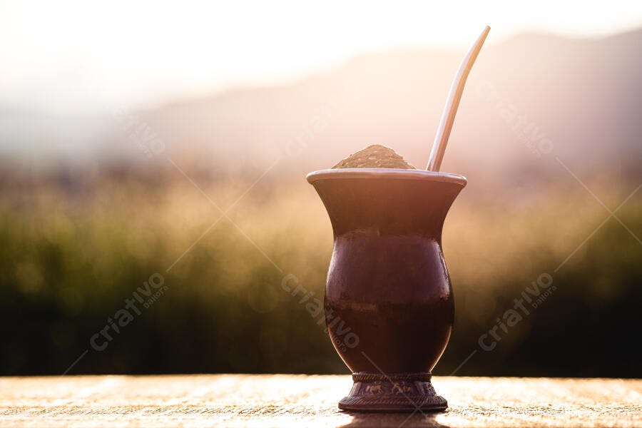 Cuia de chimarrão escura com erva-mate e bombilla ao entardecer no campo