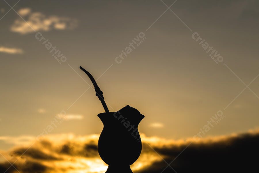 Mate chimarrão em silhueta dourada contra o pôr do sol
