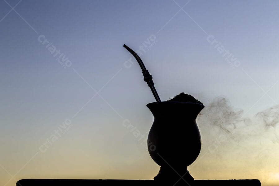 Cuia de chimarrão e bomba em silhueta no amanhecer azul e dourado