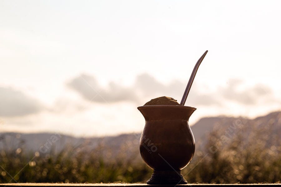 Cuia de chimarrão com bomba e erva-mate ao amanhecer em paisagem campestre dourada