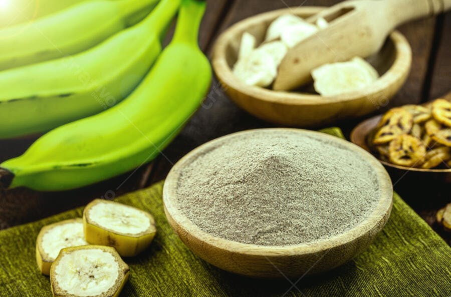 Banana verde farinha de banana e chips em tigelas rústicas sobre madeira