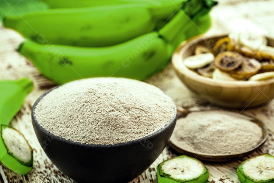 Farinha de banana verde em tigela preta com bananas frescas e rodelas secas