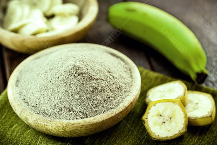 Farinha de banana verde em tigela com bananas frescas e fatiadas