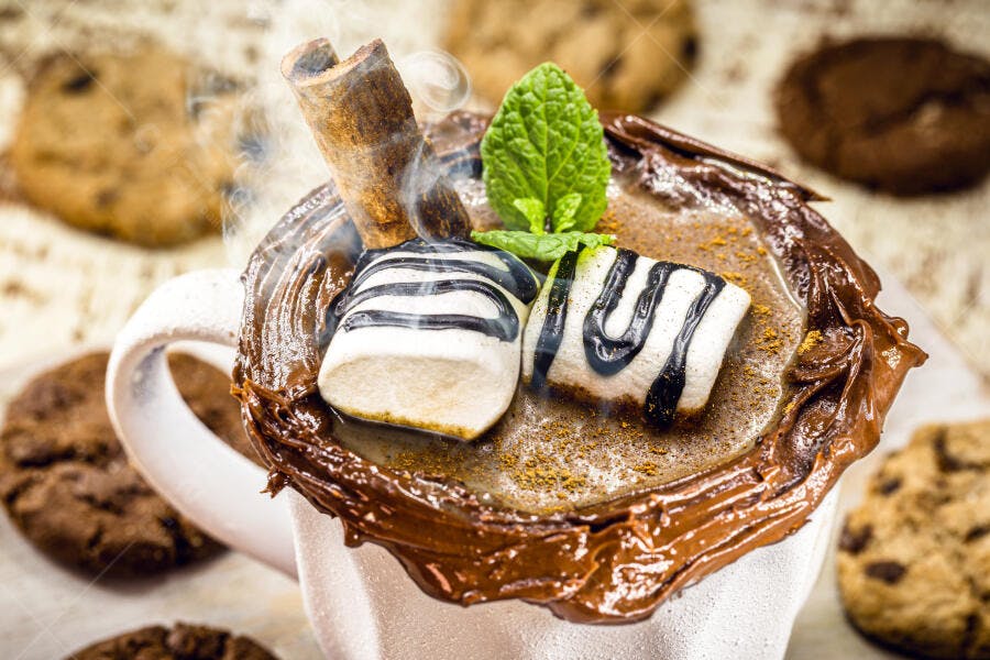 Chocolate quente cremoso com marshmallows canela e hortelã em caneca branca com biscoitos