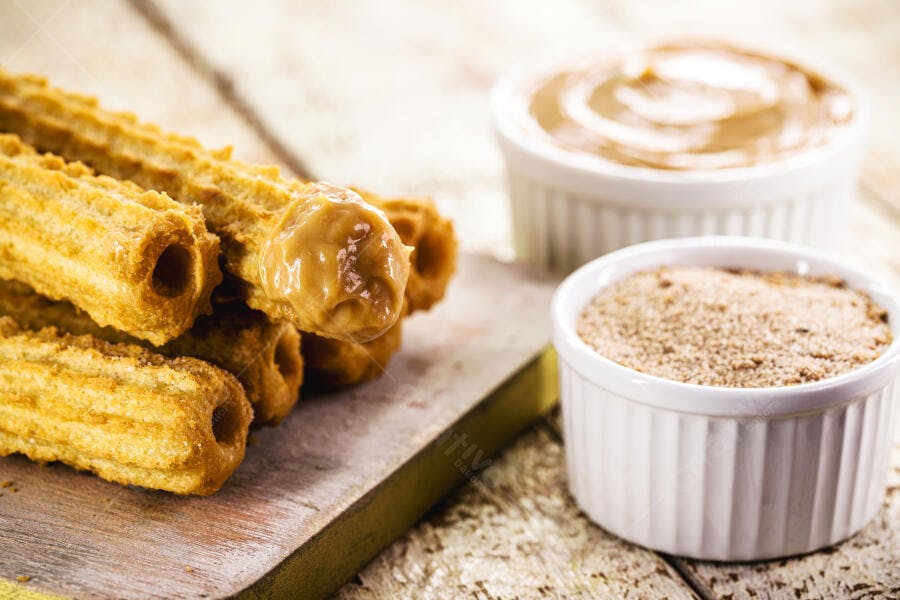 Churros dourados com doce de leite e açúcar em tábua de madeira