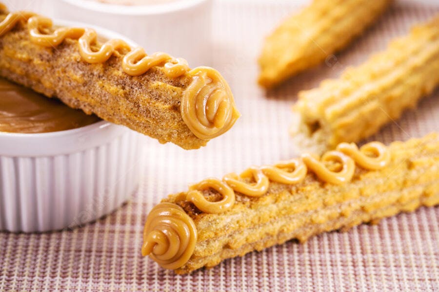 Churros crocantes com doce de leite em tigela branca