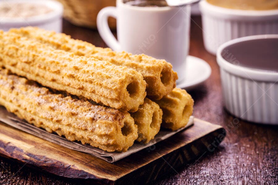 Churros dourados com açúcar em tábua de madeira e bebidas no café da tarde
