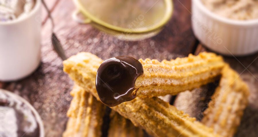 Churros crocantes cobertos com calda de chocolate em mesa rústica
