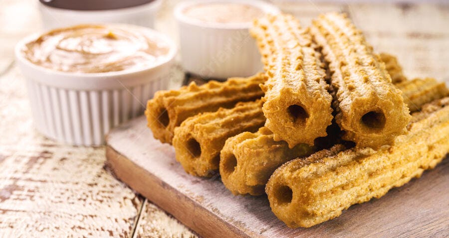 Churros crocantes dourados com açúcar e doce de leite na mesa rústica