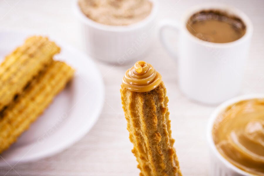 Churro com doce de leite cremoso e café em mesa clara de madeira