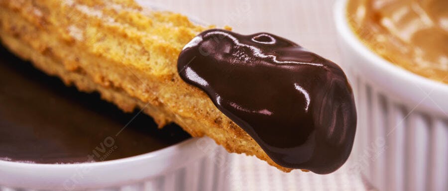 Churro dourado com chocolate derretido em prato branco sobre mesa