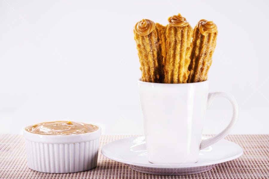 Churros crocantes com doce de leite em caneca branca e ramequim