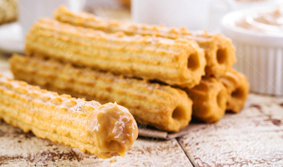 Churros doces com doce de leite e açúcar em mesa de madeira rústica