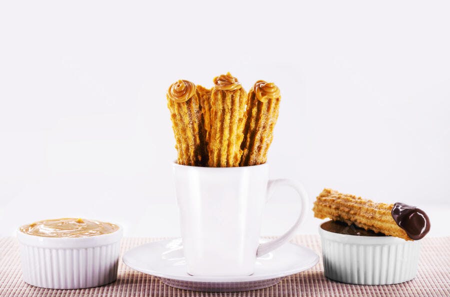Churros crocantes com doce de leite e chocolate em mesa clara