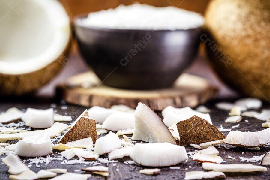 Coco ralado em tigela preta com lascas e coco fresco em madeira escura