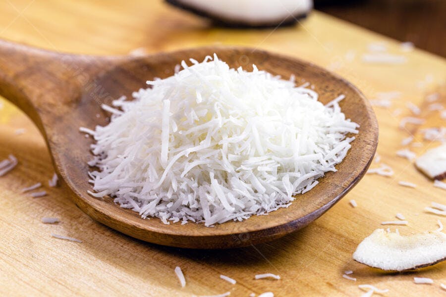 Coco ralado branco em colher de pau sobre madeira natural