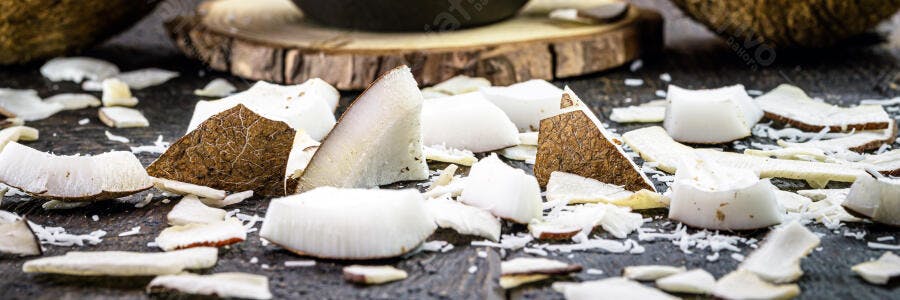 Pedaços de coco frescos e lascas em superfície rústica marrom escura