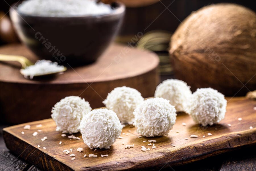Doces beijinhos de coco brancos em tábua de madeira rústica com coco ralado