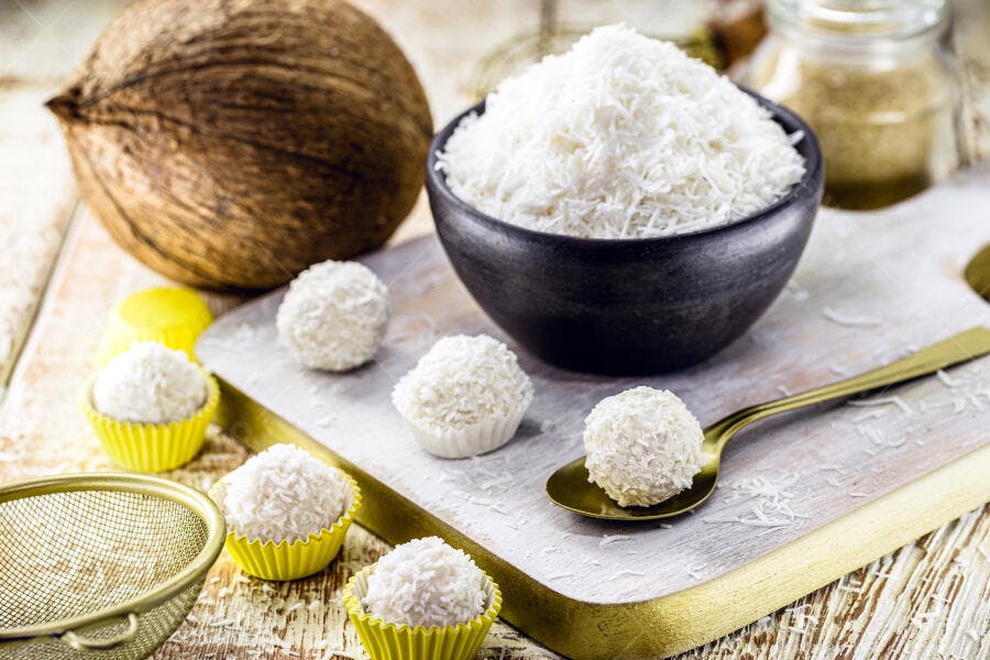 Beijinhos de coco doces e coco ralado fresco em mesa rústica