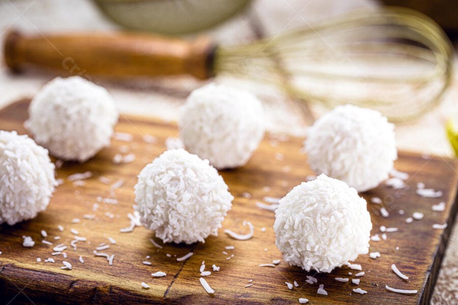 Beijinhos de coco frescos em tábua de madeira rústica com batedor de arame