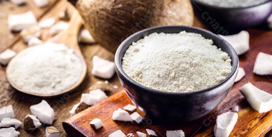 Farinha de coco em tigela e colher sobre madeira com pedaços de coco