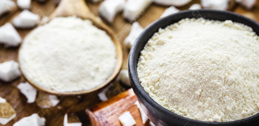 Farinha de coco branca em tigela e colher de pau com coco fresco