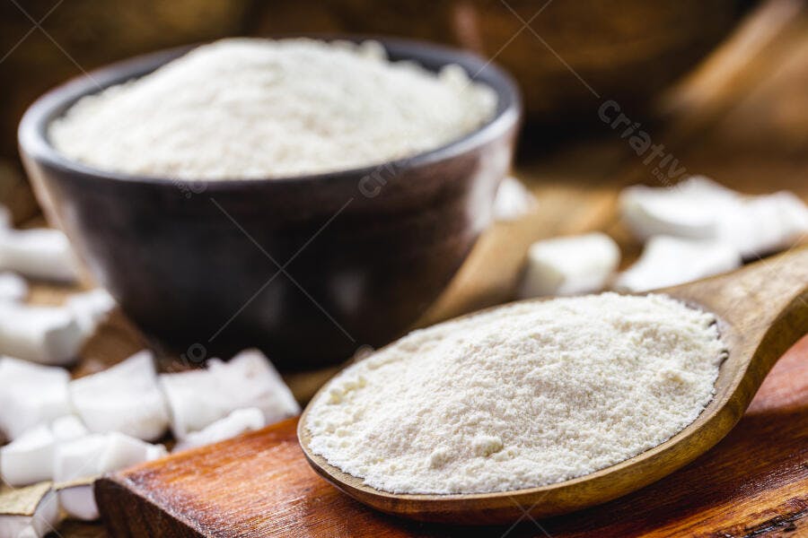 Farinha de coco branca em tigela e colher de madeira com coco fresco