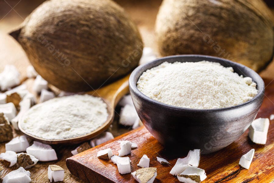 Farinha de coco branca em tigela rústica com cocos inteiros e pedaços na madeira