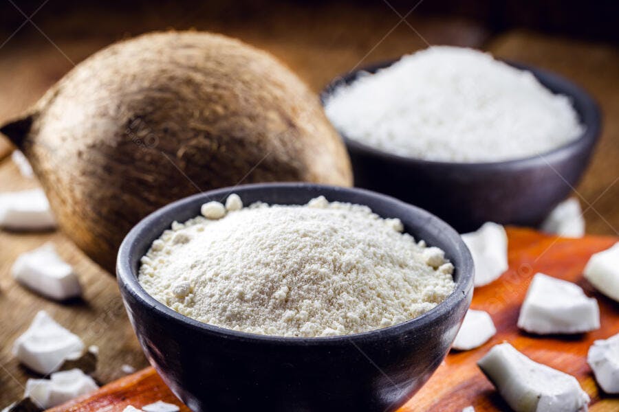 Coco inteiro farinha e ralado em tigelas pretas sobre madeira