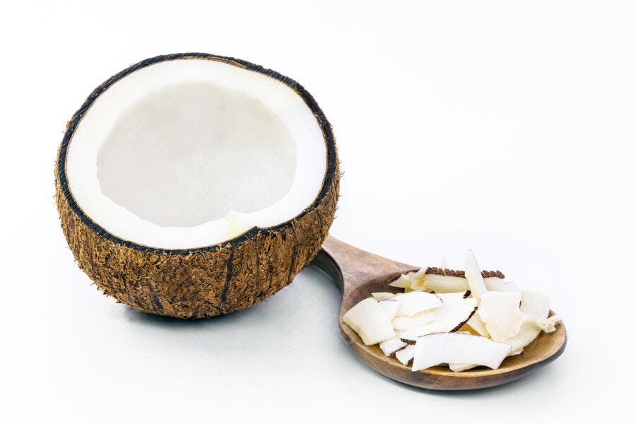 Coco fresco aberto com lascas em colher de pau em fundo branco