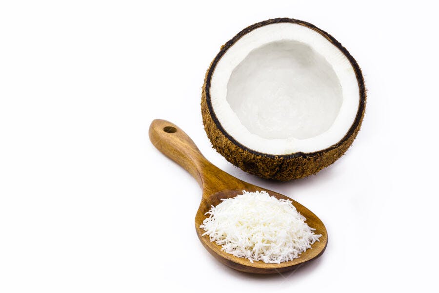 Coco fresco e ralado em colher de madeira sobre fundo branco