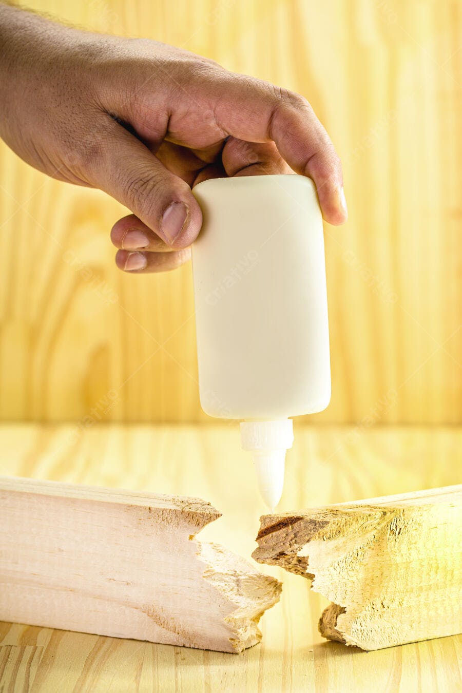 Mão aplicando cola branca em madeira quebrada sobre superfície de pinho