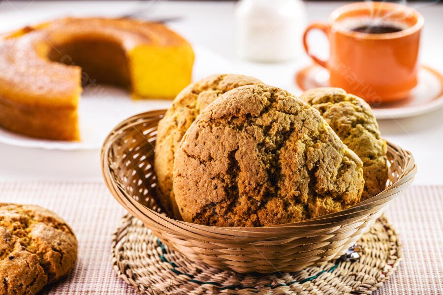 Biscoitos caseiros em cesta com bolo de fubá e café fumegante na mesa de café