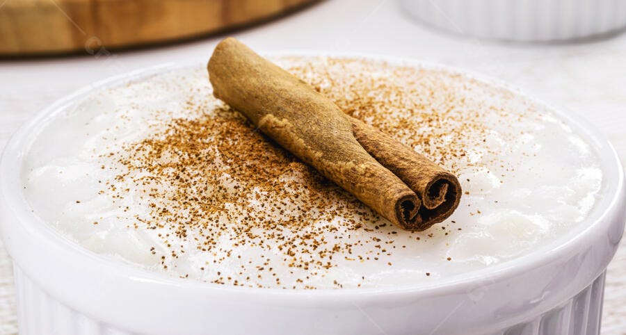 Arroz doce cremoso com canela em pau e pó em tigela branca