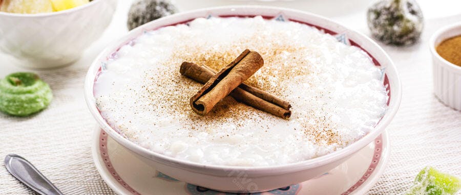 Arroz doce cremoso com canela em pau e em pó sobre mesa branca