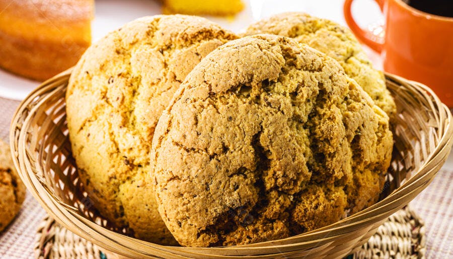 Biscoitos caseiros dourados em cesta de vime com xícara de café ao fundo