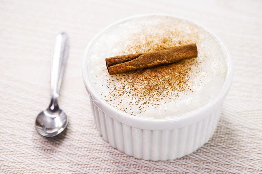 Arroz doce cremoso em tigela branca com canela em pau e pó e colher de prata