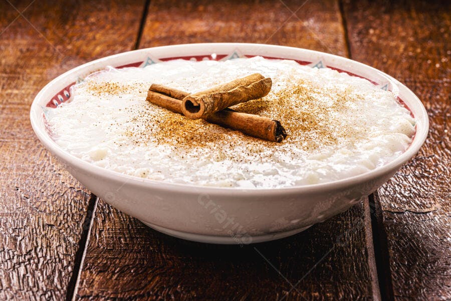Arroz doce cremoso com canela em pau e pó em tigela branca na mesa rústica