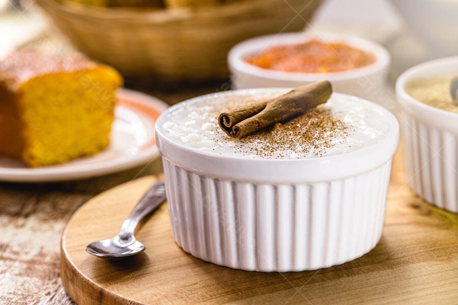 Arroz doce branco cremoso com canela em tigela na tábua de madeira e bolo
